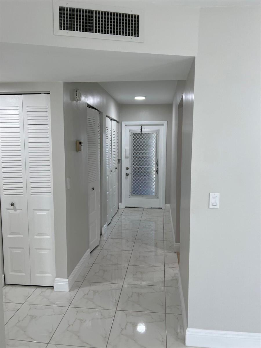A hallway with white tile flooring leads to a white front door with a screen — 24 Abbey Lane # 204, Delray Beach FL 33446, DELRAY BEACH, FL