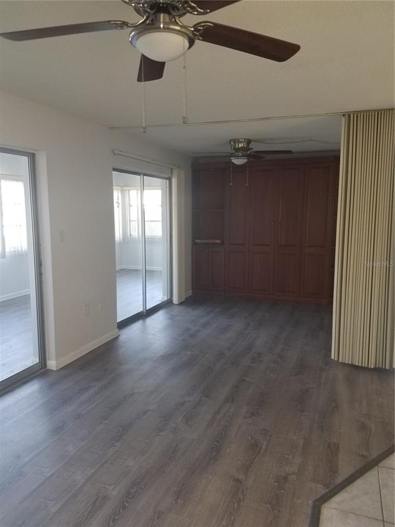 A living room features wood-look flooring, a ceiling fan, sliding glass doors, and built-in cabinetry — 4854 MARINE PARKWAY UNIT 103, NEW PORT RICHEY, FL