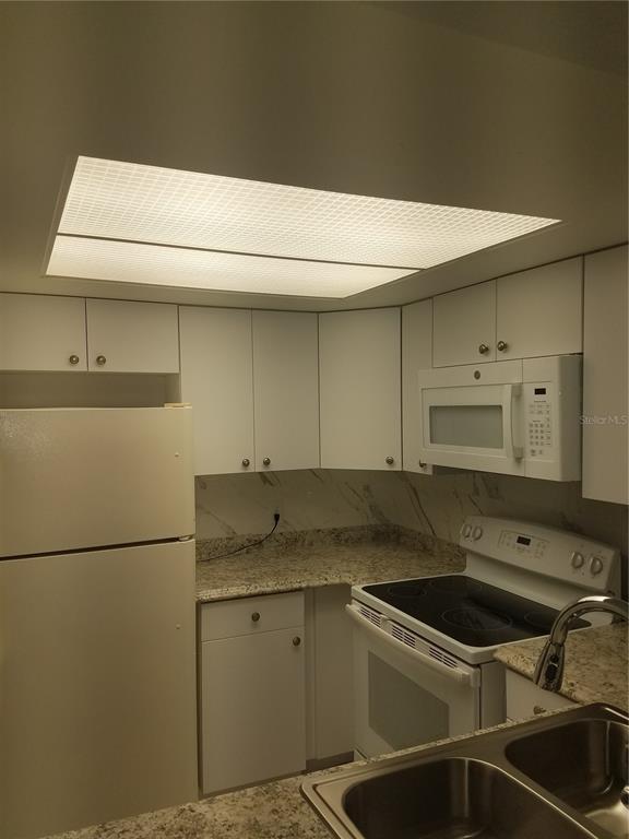 A kitchen features white cabinets, granite countertops, a white refrigerator, and a built-in microwave — 4854 MARINE PARKWAY UNIT 103, NEW PORT RICHEY, FL