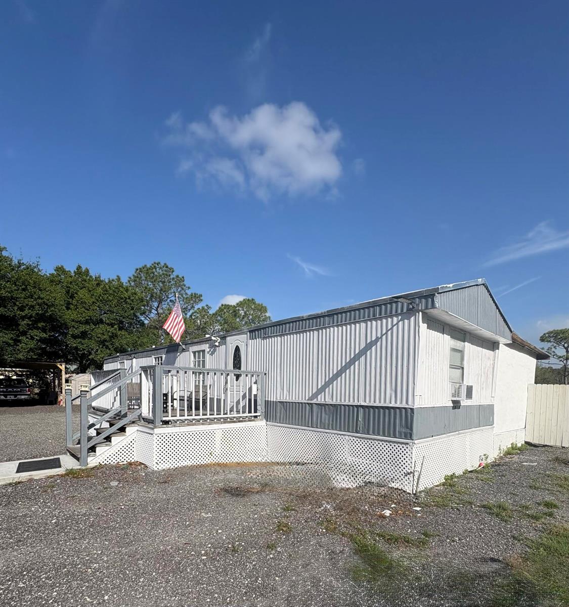 A single-story mobile home with a wooden deck and an American flag under a sky — 187 Montura Avenue, Clewiston FL 33440, CLEWISTON, FL