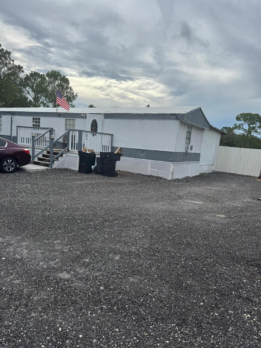 A single-story mobile home with a front deck, American flag, and gravel driveway — 187 Montura Avenue, Clewiston FL 33440, CLEWISTON, FL