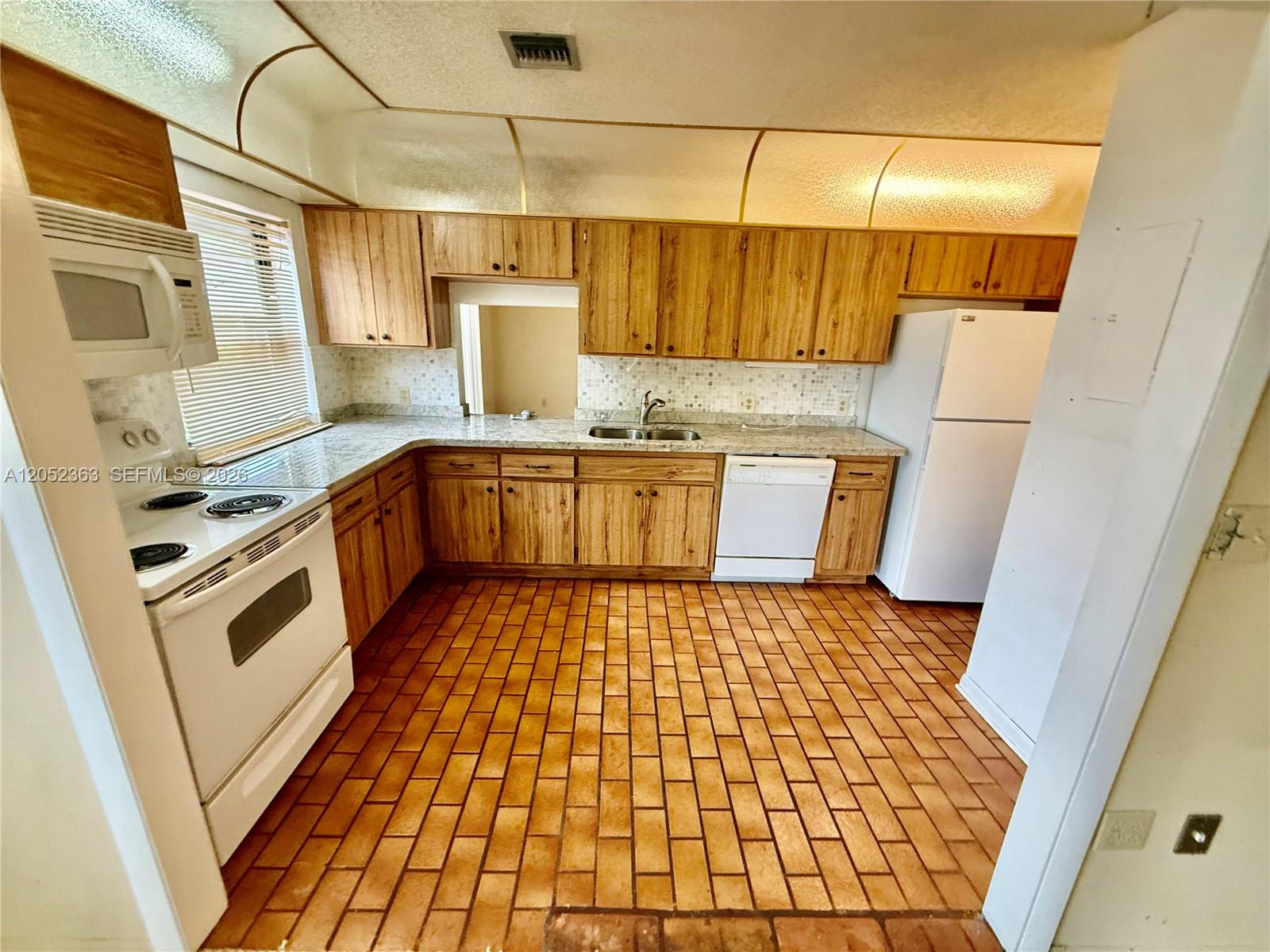 A kitchen features wood cabinets, white appliances, a tiled backsplash, and brick-style flooring — 3620 Farragut St, Hollywood FL 33021, HOLLYWOOD, FL