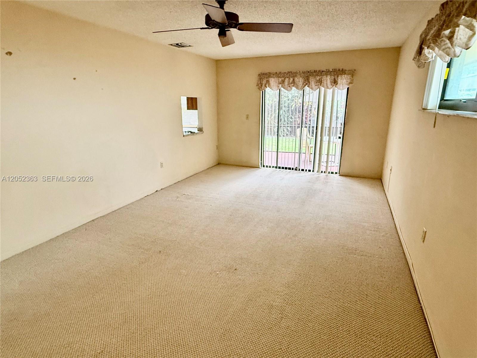 A carpeted living room features a ceiling fan, a small wall cutout, and sliding glass doors — 3620 Farragut St, Hollywood FL 33021, HOLLYWOOD, FL