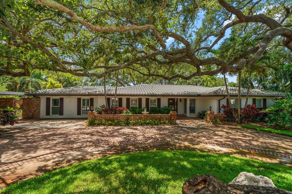 A single-story house with a brick driveway and mature oak trees in the front yard — 7 ROSERY LANE, BELLEAIR, FL
