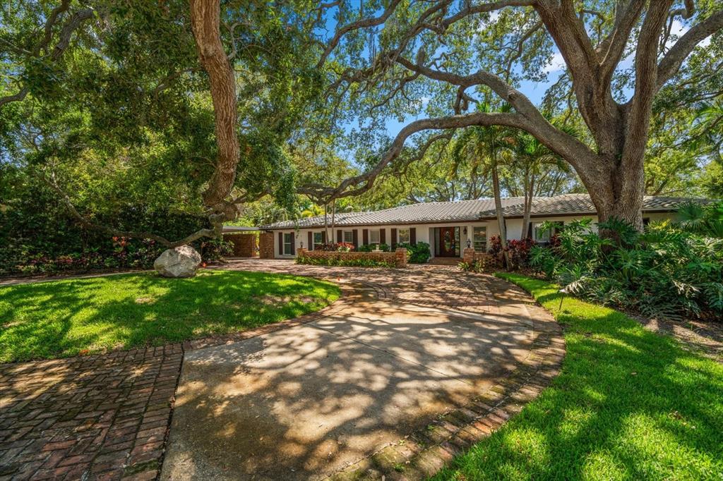 A single-story house with a brick-paved driveway sits under large, mature oak trees — 7 ROSERY LANE, BELLEAIR, FL