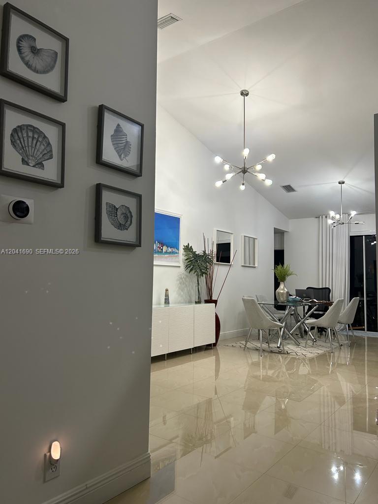 A bright dining area features a modern chandelier, glass table, and white tiled flooring — 805 Falling Water Rd, Weston FL 33326, WESTON, FL