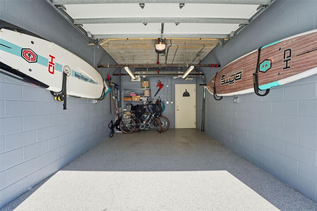 A garage with gray block walls, epoxy flooring, and two paddleboards mounted on the walls — 1350 5TH STREET UNIT 402, SARASOTA, FL