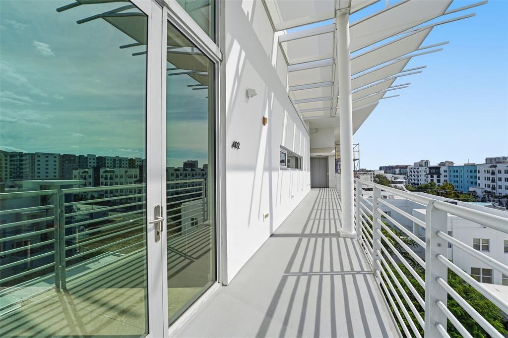 A modern apartment balcony features white walls, a metal railing, and a slatted overhead canopy — 1350 5TH STREET UNIT 402, SARASOTA, FL