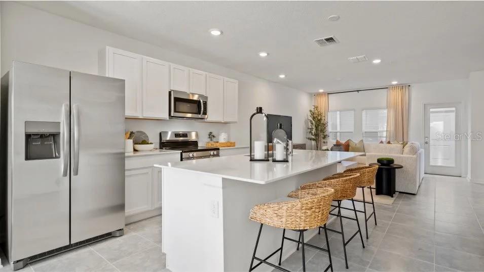 A modern kitchen features white cabinets, stainless steel appliances, and a large island with stools — 11309 RISING SUN STREET, ORLANDO, FL