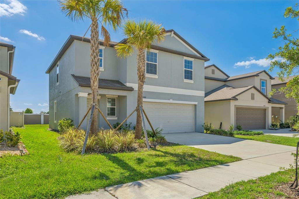 A two-story suburban house with a light gray exterior, a two-car garage, and two palm trees — 11000 RADIANT SHORE LOOP, SAN ANTONIO, FL