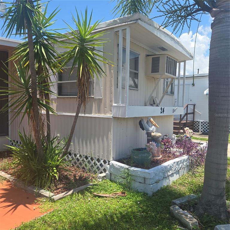 The exterior of a mobile home features a window air conditioning unit and landscaping — 27466 US HIGHWAY 19 N UNIT 24, CLEARWATER, FL