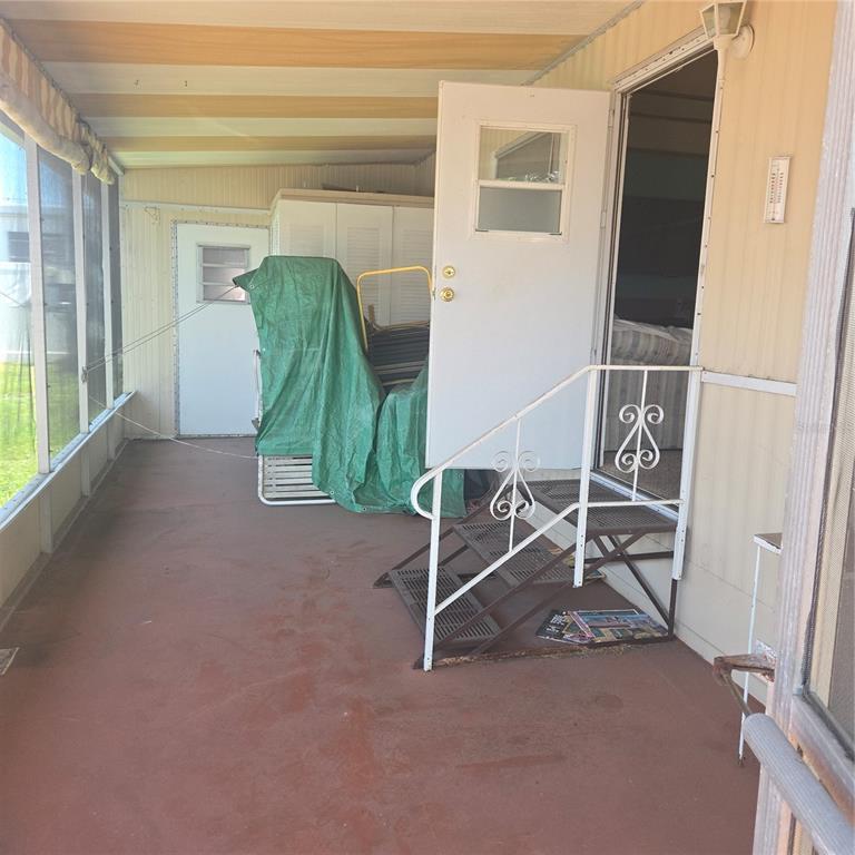 A screened-in porch features a concrete floor, metal stairs, and a white entry door — 27466 US HIGHWAY 19 N UNIT 24, CLEARWATER, FL