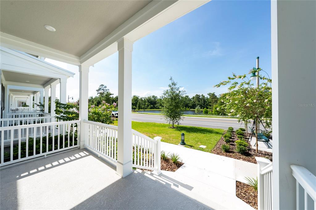 A covered front porch features white railings and columns overlooking a street and pond — 2414 CELEBRATION BOULEVARD, KISSIMMEE, FL
