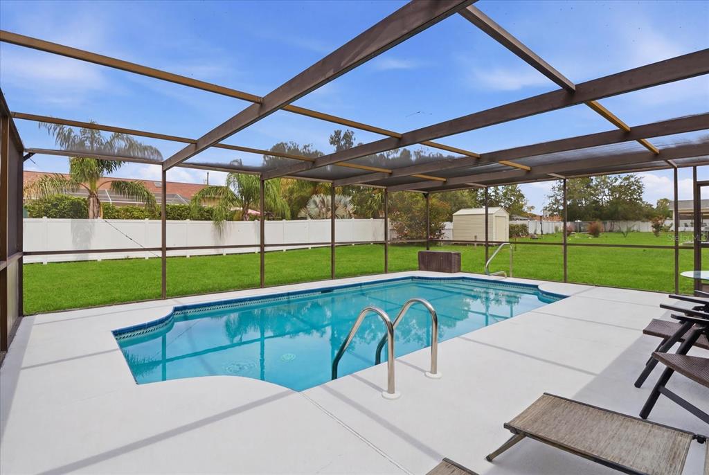 A swimming pool with a metal ladder sits inside a screened-in patio overlooking a yard — 1393 HATHAWAY AVENUE, SPRING HILL, FL
