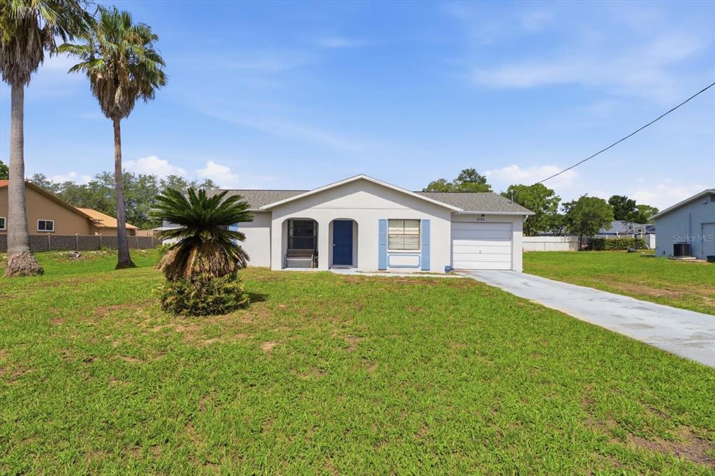 A single-story house with a white exterior, a garage, and palm trees in the yard — 1393 HATHAWAY AVENUE, SPRING HILL, FL