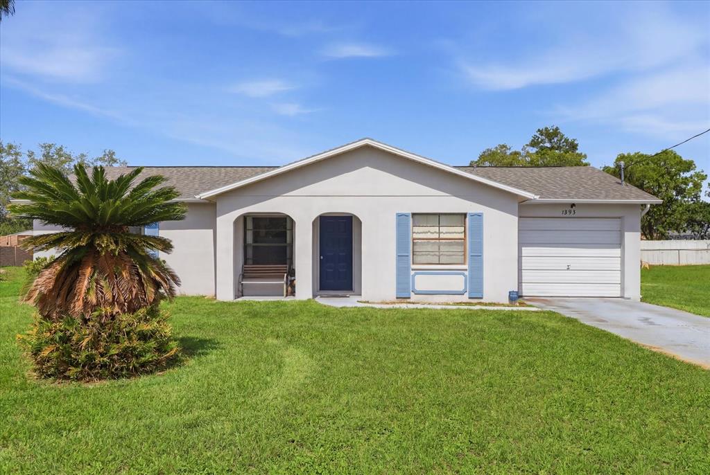 A single-story house with a light-colored exterior, blue shutters, and a front-facing garage — 1393 HATHAWAY AVENUE, SPRING HILL, FL