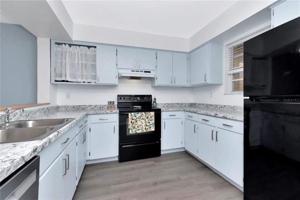 A kitchen features light blue cabinets, granite-look countertops, and black appliances — 6817 STONES THROW CIRCLE N UNIT 17203, ST PETERSBURG, FL