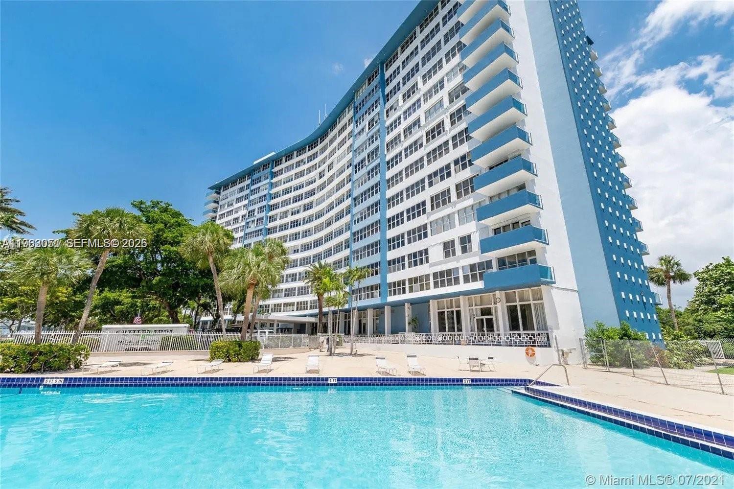 A large multi-story apartment building stands behind a swimming pool on a sunny day — 7441 Wayne Ave # 9I, Miami Beach FL 33141, MIAMI BEACH, FL