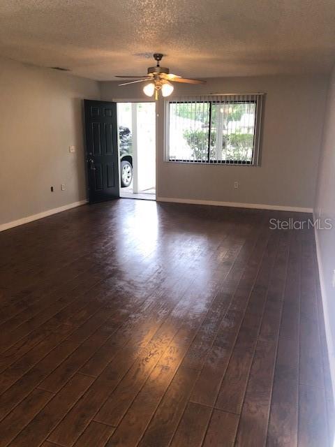 A living room with dark wood-look flooring, a ceiling fan, and an open front door — 810 E 20TH STREET, SANFORD, FL