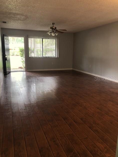 An empty living room features wood-look flooring, a ceiling fan, and a door leading outside — 810 E 20TH STREET, SANFORD, FL