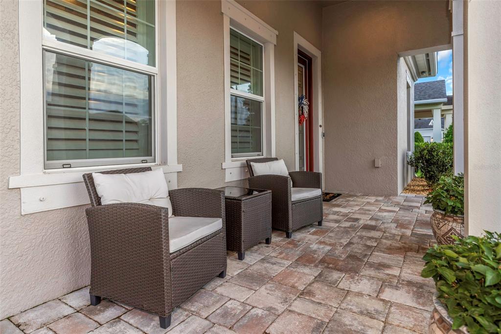 A covered front porch features two wicker chairs, a small table, and paver flooring — 4042 WOODLAND RETREAT BOULEVARD, NEW PORT RICHEY, FL
