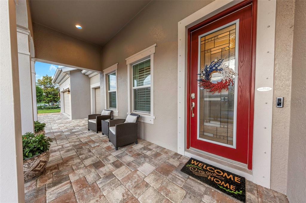 A covered porch features a red front door, two wicker chairs, and a paved floor — 4042 WOODLAND RETREAT BOULEVARD, NEW PORT RICHEY, FL