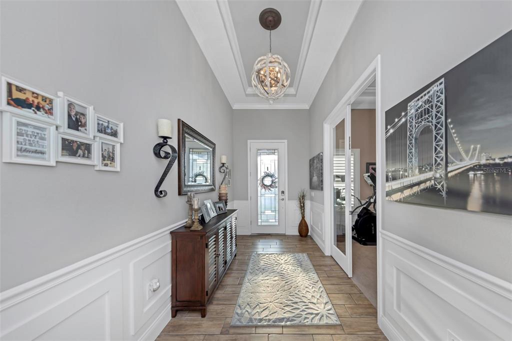 A bright entryway features a wood-toned console table, a patterned rug, and a coffered ceiling — 4042 WOODLAND RETREAT BOULEVARD, NEW PORT RICHEY, FL