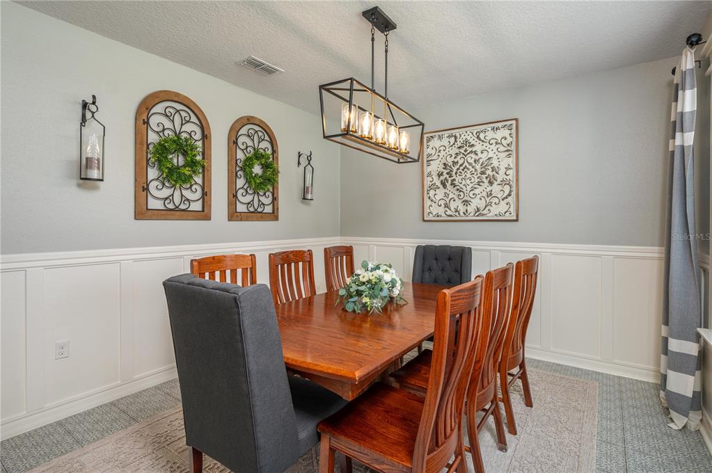 A dining room with wainscoting, a wooden table, and chairs sits beside an arched entryway — 863 LAKE CUMMINGS BOULEVARD, LAKE ALFRED, FL
