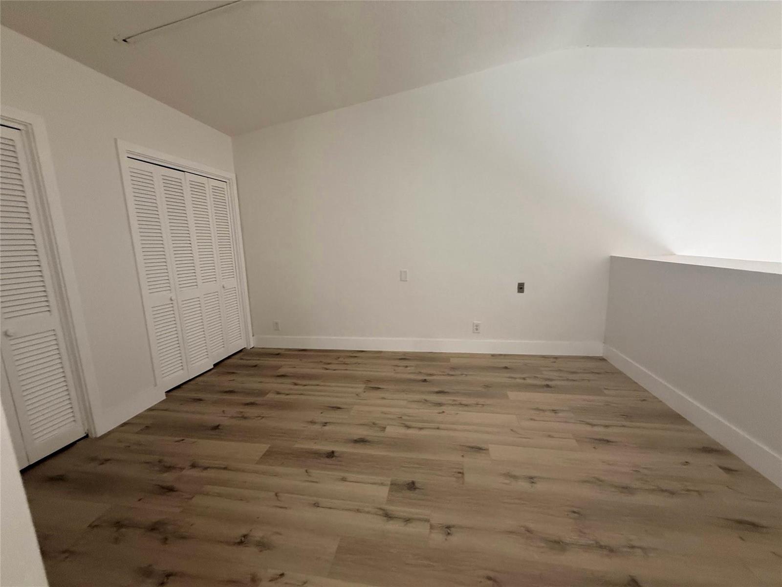 An empty room with white walls, light wood-look flooring, and white louvered closet doors — 811 E Broward Boulevard, Fort Lauderdale FL 33301, FORT LAUDERDALE, FL