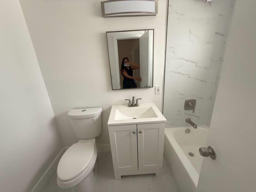 A bathroom featuring a white vanity, a toilet, and a bathtub with marble-look wall tiles — 811 E Broward Boulevard, Fort Lauderdale FL 33301, FORT LAUDERDALE, FL