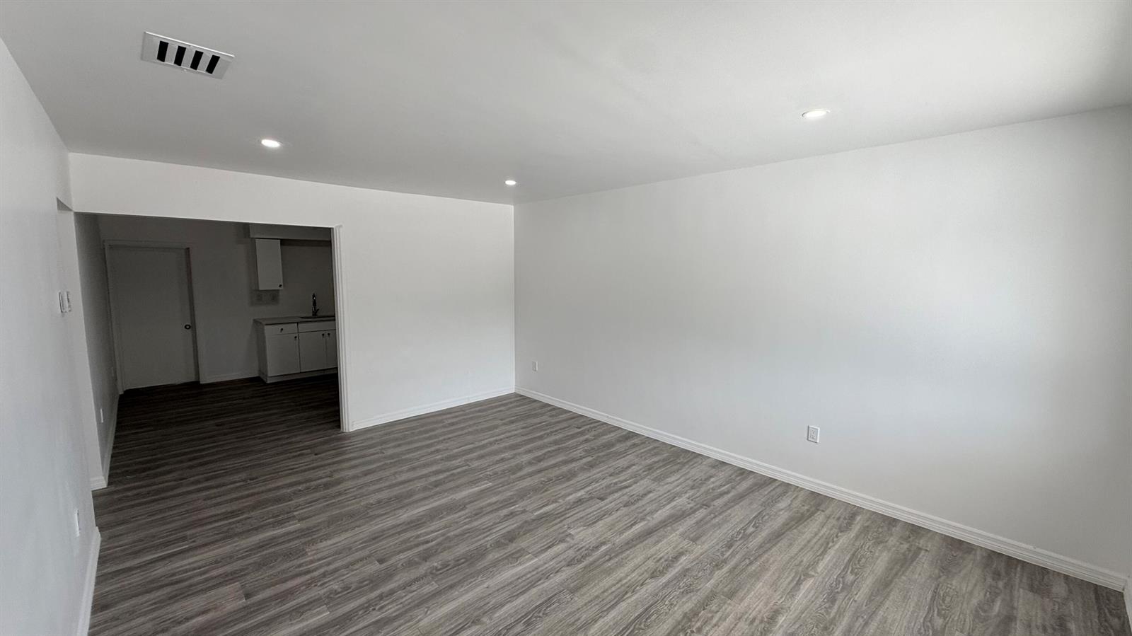An empty room with gray wood-look flooring and white walls leads into a kitchen area — 1063 NW 108th Terrace, Miami FL 33168, MIAMI, FL