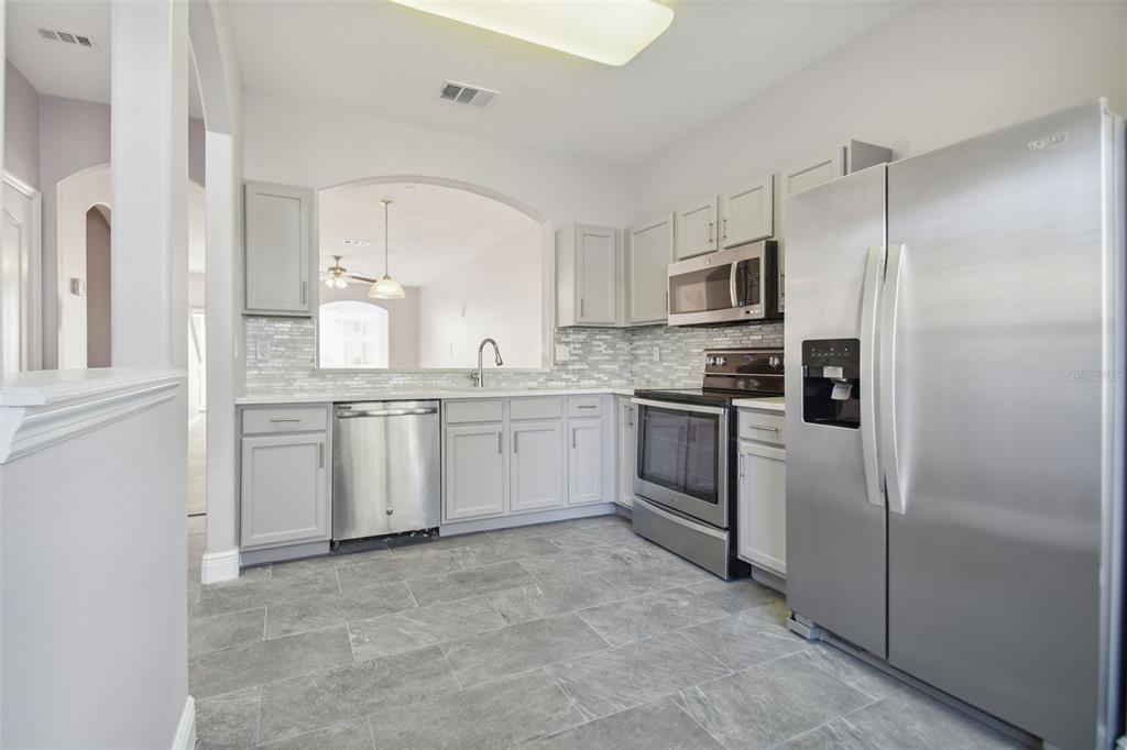 A kitchen with gray cabinets, stainless steel appliances, a tile backsplash, and gray floor tiles — 3430 HIGH HAMPTON CIRCLE, TAMPA, FL