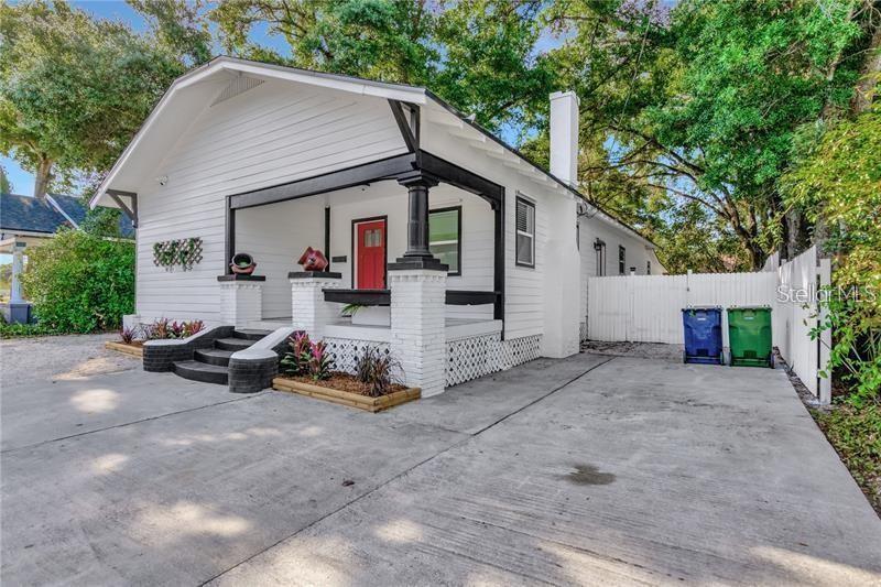 A white bungalow with a black-trimmed front porch, red door, and concrete driveway — 705 E PLYMOUTH STREET, TAMPA, FL