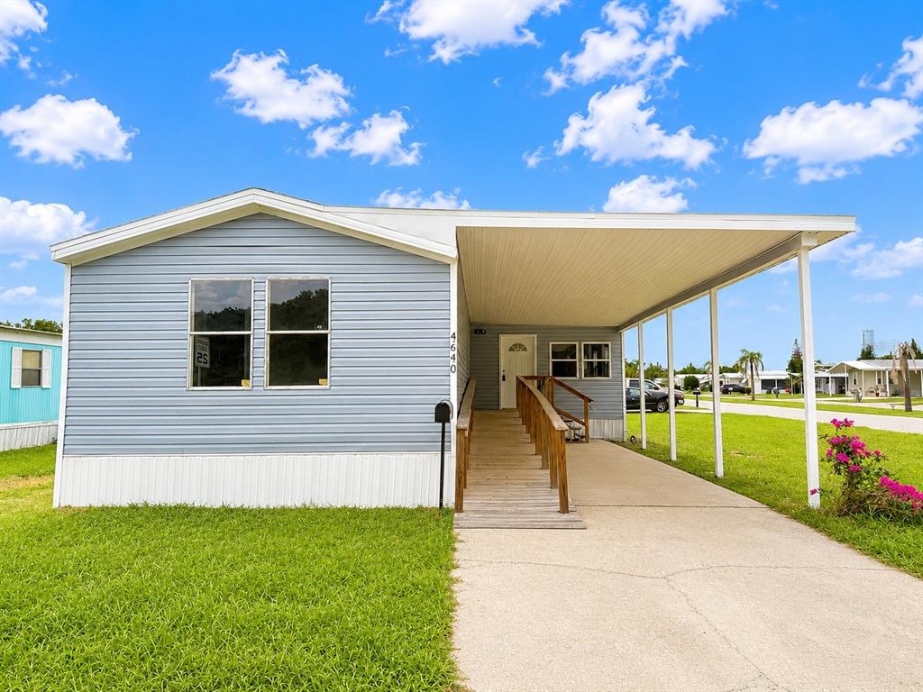 A light blue mobile home features a carport, a wooden ramp, and a concrete driveway — 4640 CALOOSA BOULEVARD, LAKE WALES, FL