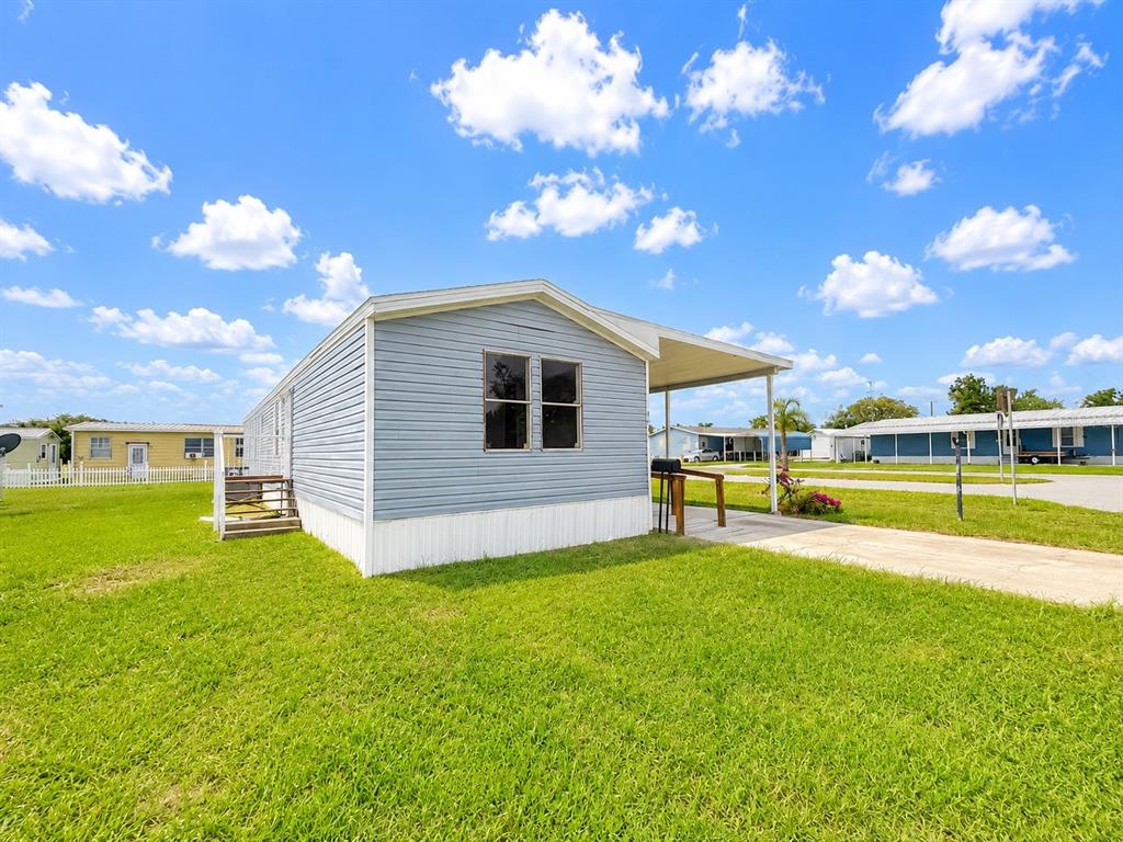 A light blue mobile home with a carport sits on a grassy lot under clouds — 4640 CALOOSA BOULEVARD, LAKE WALES, FL