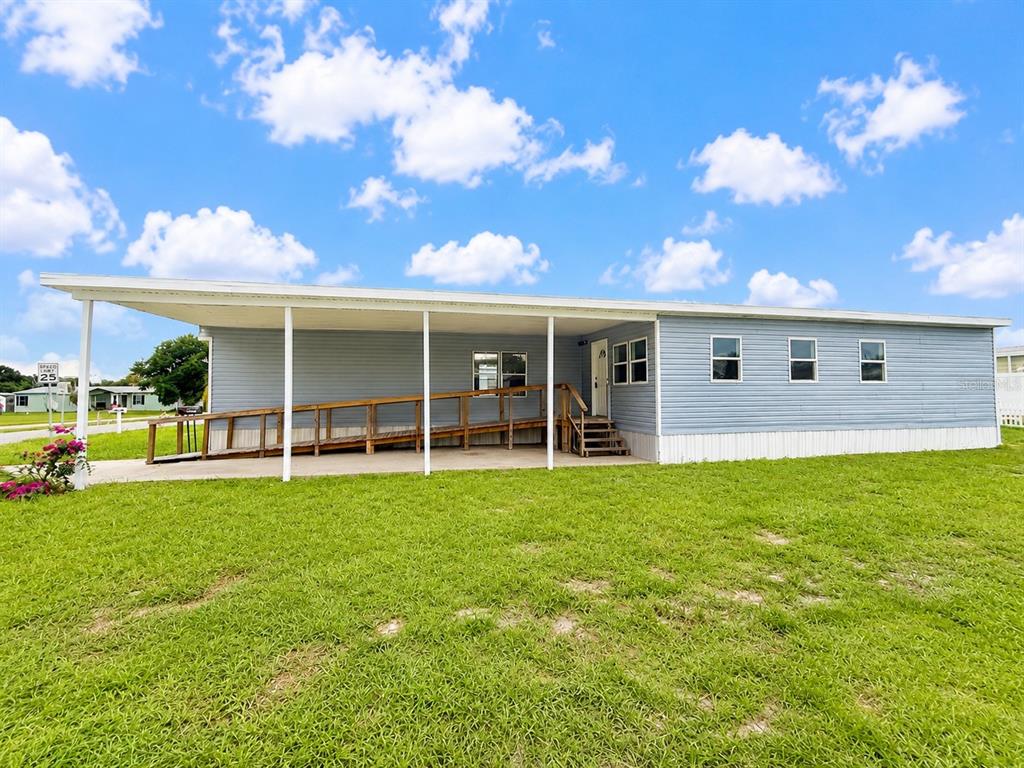 A light blue mobile home with a large covered porch and a wooden wheelchair ramp — 4640 CALOOSA BOULEVARD, LAKE WALES, FL