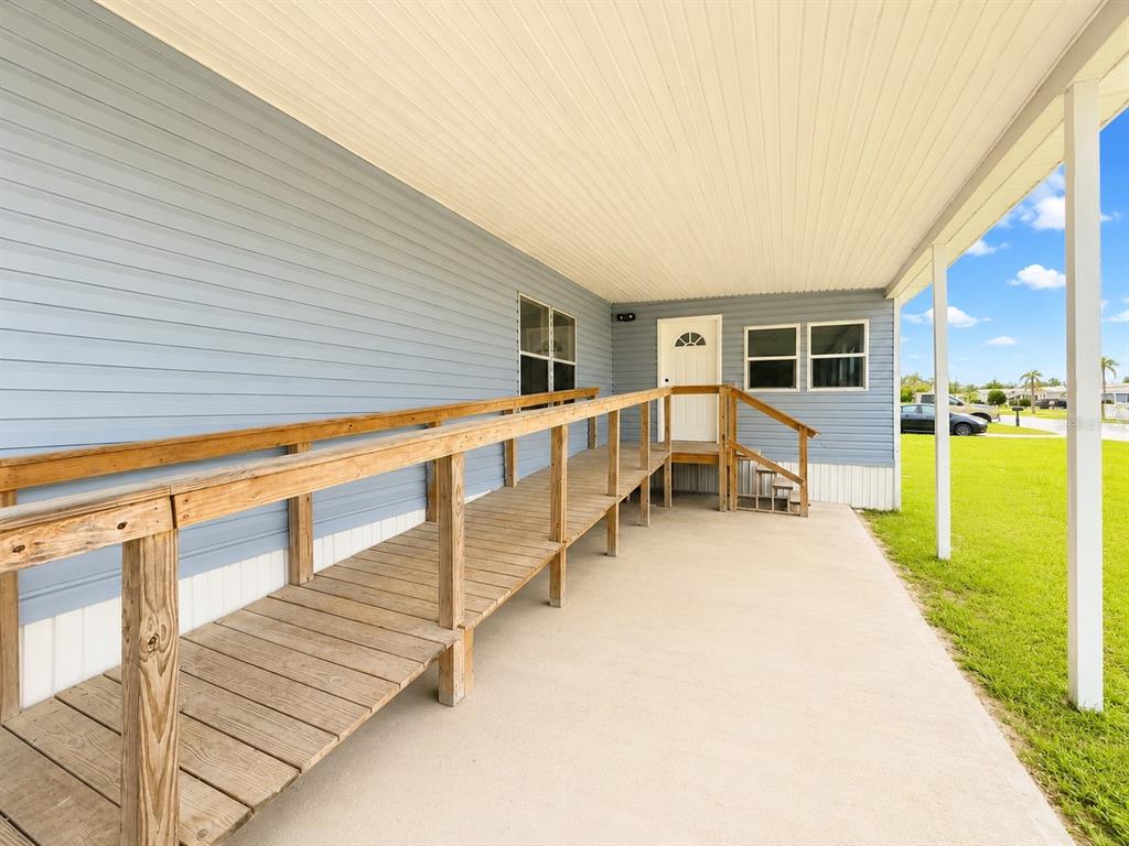 A light blue mobile home exterior features a wooden wheelchair ramp leading to the front door — 4640 CALOOSA BOULEVARD, LAKE WALES, FL