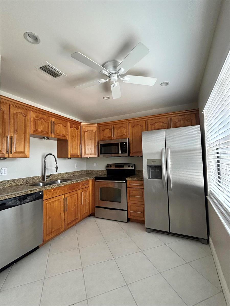 A kitchen featuring wood cabinets, granite countertops, stainless steel appliances, and a ceiling fan — 16415 Berry Way, Delray Beach FL 33484, DELRAY BEACH, FL