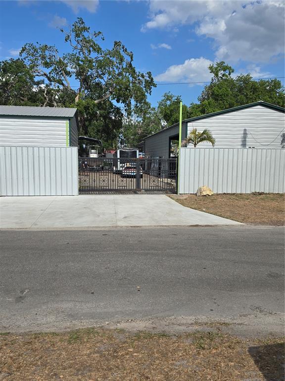A gated driveway sits between two metal-sided buildings with a concrete approach from the street — 5823 BARRY LANE, TAMPA, FL