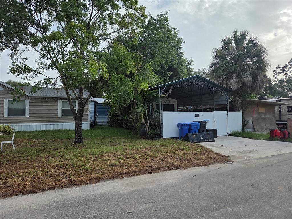 A mobile home with a carport and a white fence sits on a grassy lot — 5823 BARRY LANE, TAMPA, FL