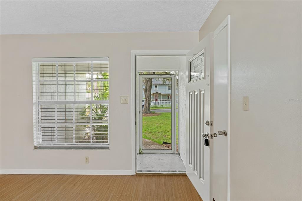 An interior view of a room with wood-look flooring, a window with blinds, and an open door — 125 N RHODES STREET, MOUNT DORA, FL