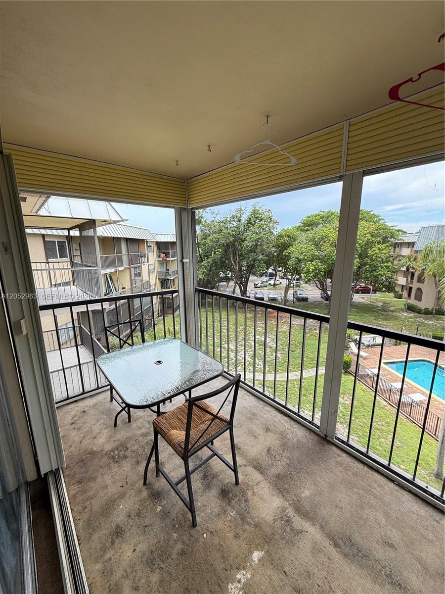 A screened-in balcony features a glass-top table, a single chair, and a view of a pool — 5961 N Falls Cir Dr # 408, Lauderhill FL 33319, LAUDERHILL, FL