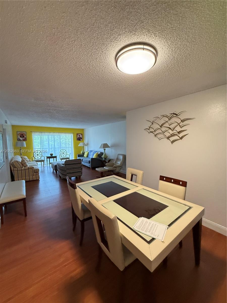 A dining area with a glass-topped table leads into a living room with yellow walls — 5961 N Falls Cir Dr # 408, Lauderhill FL 33319, LAUDERHILL, FL