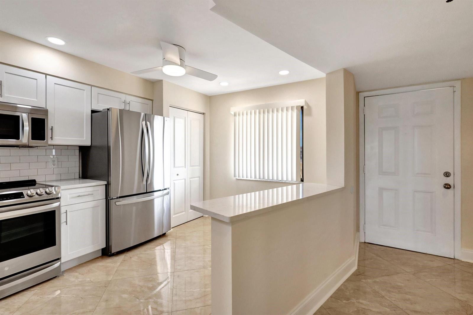A kitchen with white cabinets, stainless steel appliances, a breakfast bar, and tile flooring — 14460 Strathmore Lane # 807, Delray Beach FL 33446, DELRAY BEACH, FL