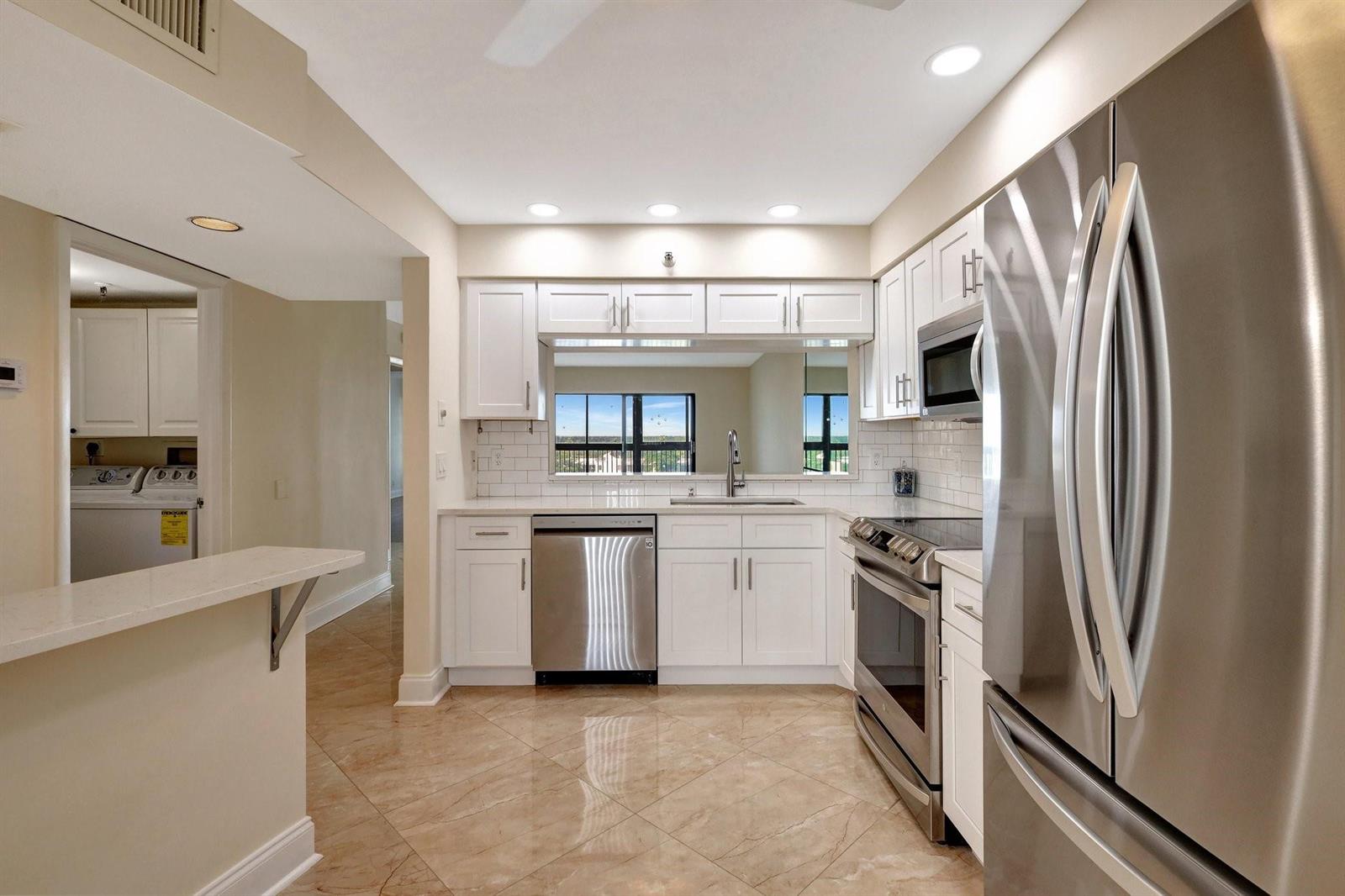 A kitchen with white cabinets, stainless steel appliances, quartz countertops, and light-colored tile flooring — 14460 Strathmore Lane # 807, Delray Beach FL 33446, DELRAY BEACH, FL