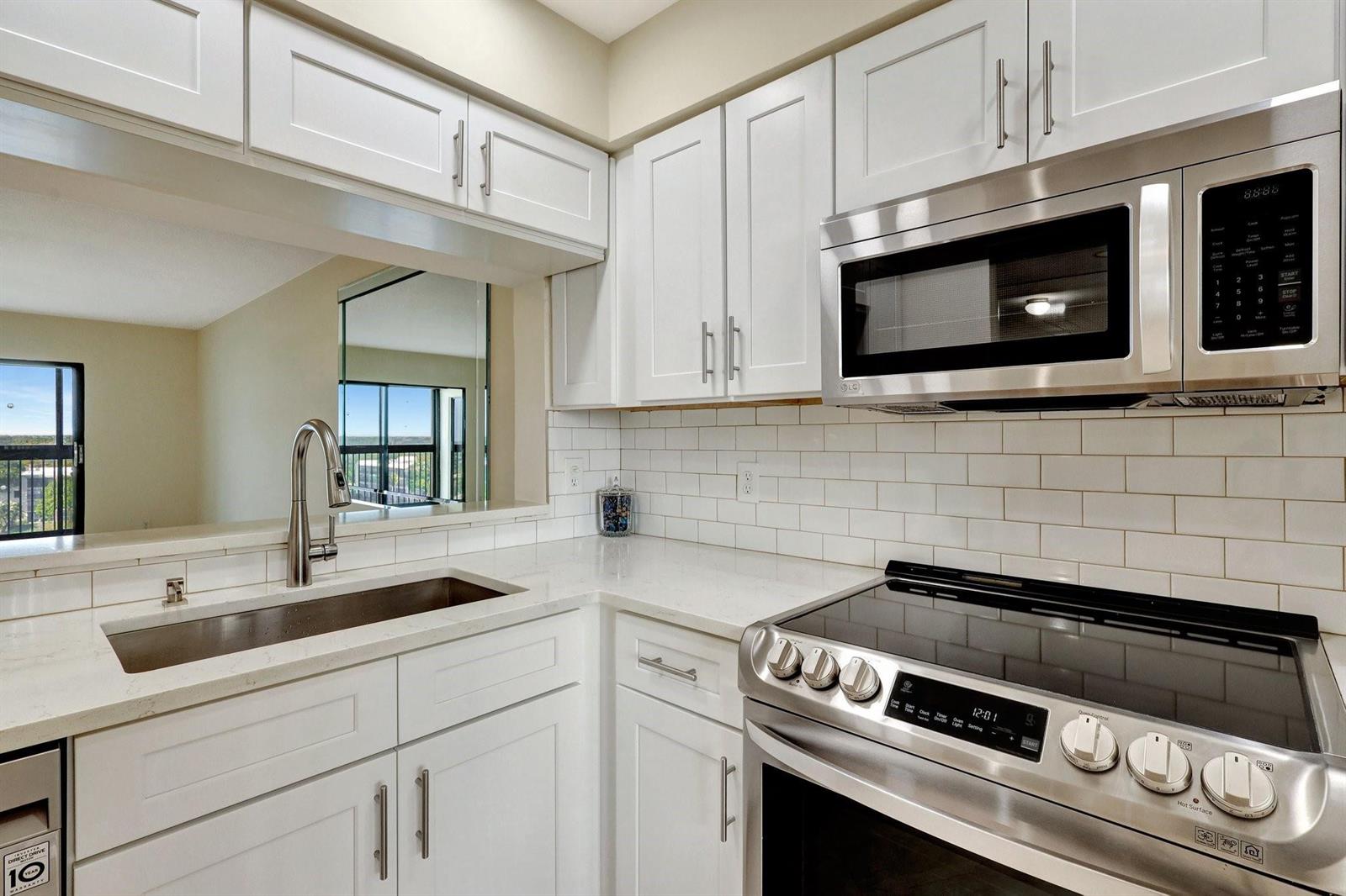 A kitchen features white cabinets, stainless steel appliances, white subway tile, and a sink — 14460 Strathmore Lane # 807, Delray Beach FL 33446, DELRAY BEACH, FL