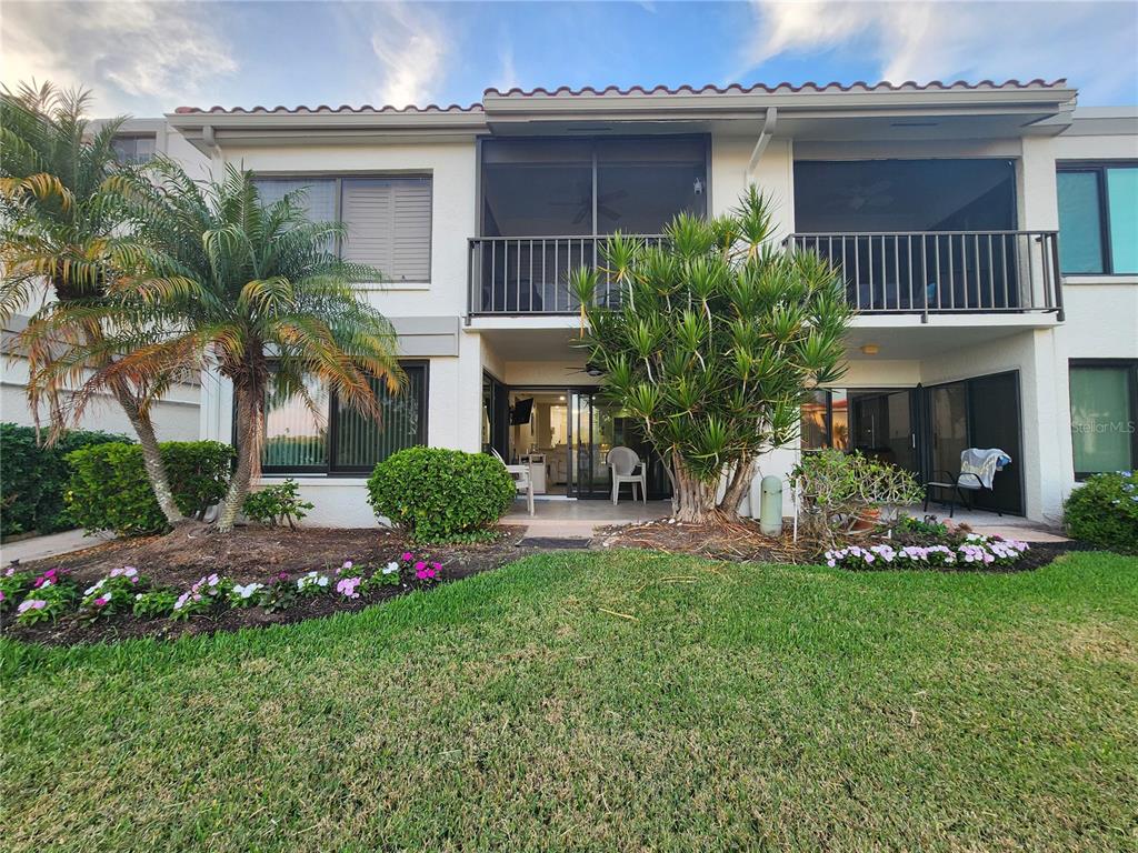 A two-story residential building features a ground-level patio, a screened upper balcony, and landscaping — 6361 BAHIA DEL MAR BOULEVARD UNIT 104, ST PETERSBURG, FL