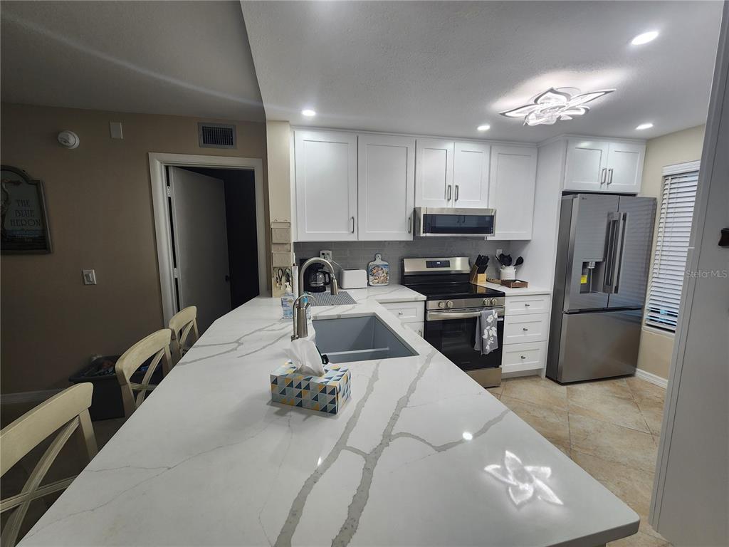 A kitchen features white cabinets, stainless steel appliances, and a large quartz-topped island — 6361 BAHIA DEL MAR BOULEVARD UNIT 104, ST PETERSBURG, FL