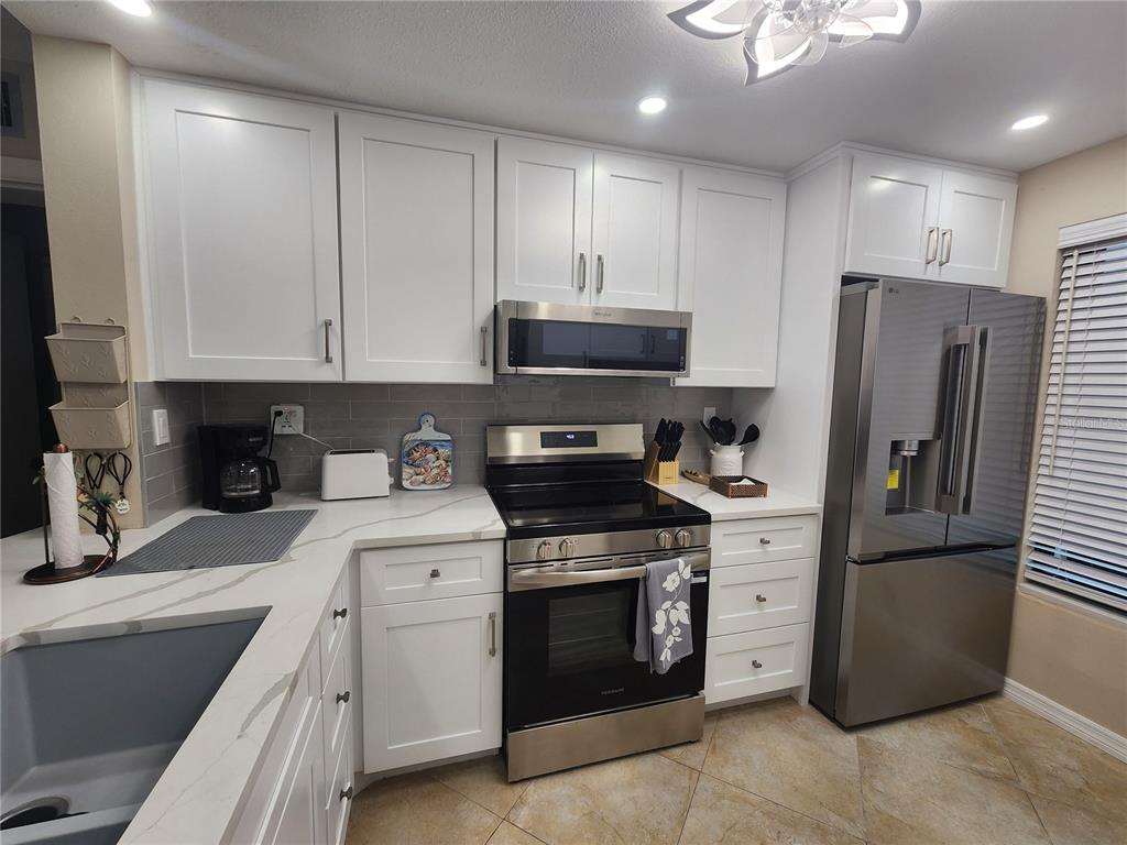 A kitchen features white cabinets, stainless steel appliances, gray tile backsplash, and quartz countertops — 6361 BAHIA DEL MAR BOULEVARD UNIT 104, ST PETERSBURG, FL
