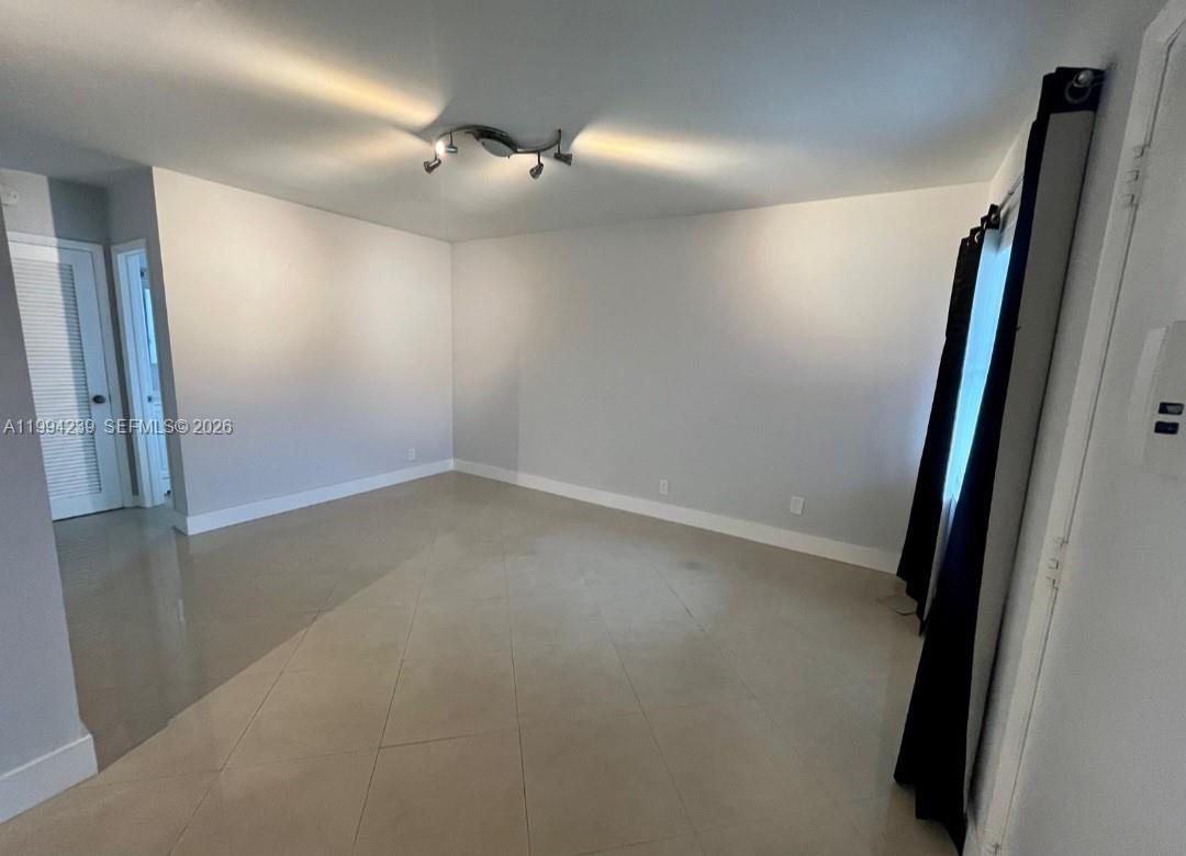 An empty room features light-colored tile flooring, white walls, and a modern ceiling light fixture — 1824 Monroe St # 14, Hollywood FL 33020, HOLLYWOOD, FL